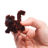 Hand holding a small, brown fuzzy pipe cleaner animal with sticker eyes on a white background.
