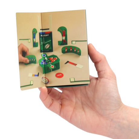 Hand holding open a mini booklet showing setup instructions for a miniature rugby match game.