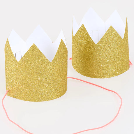 Two mini gold glitter party crowns with pink elastic straps on a white background.