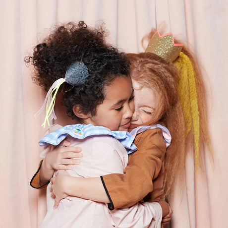 Two young girls hugging, with one wearing a mini gold glitter crown in her hair.