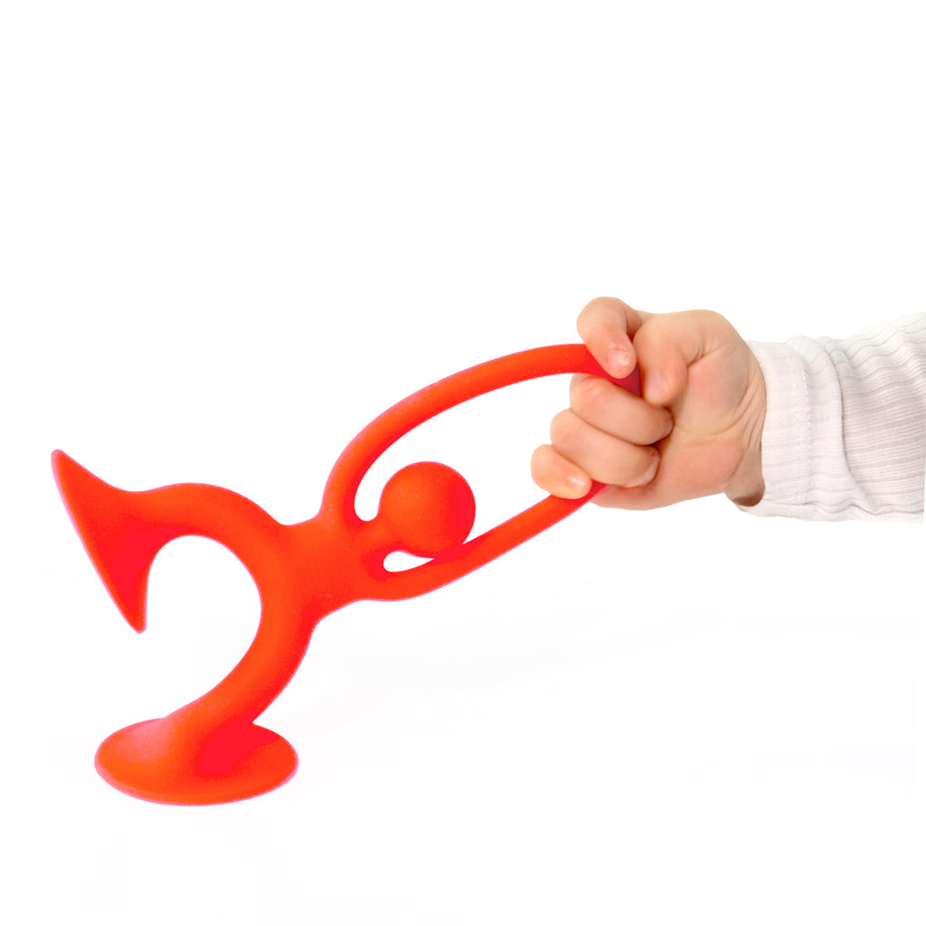 A small hand grips a bright red, abstract figure resembling a person with a trumpet. The figure stands on a flat base against a white background.