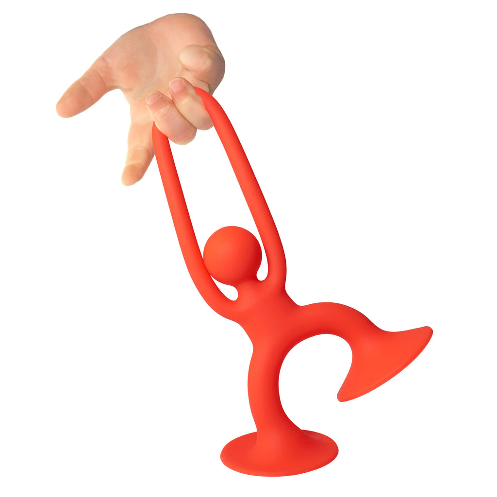 A small hand grips a bright red, abstract figure resembling a person with a trumpet. The figure stands on a flat base against a white background.
