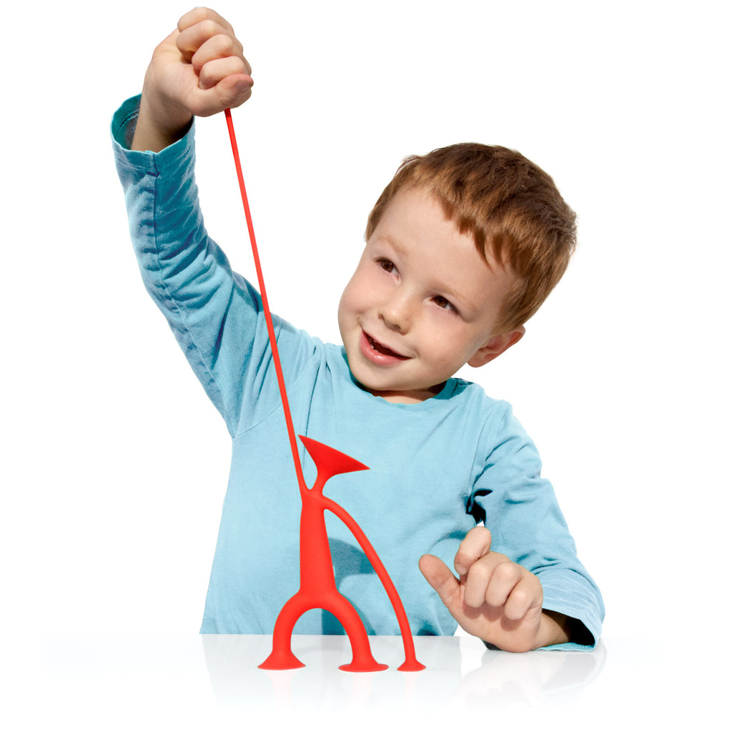 A young child in a blue shirt excitedly stretches a red, flexible toy figure with a playful expression, set against a plain white background.