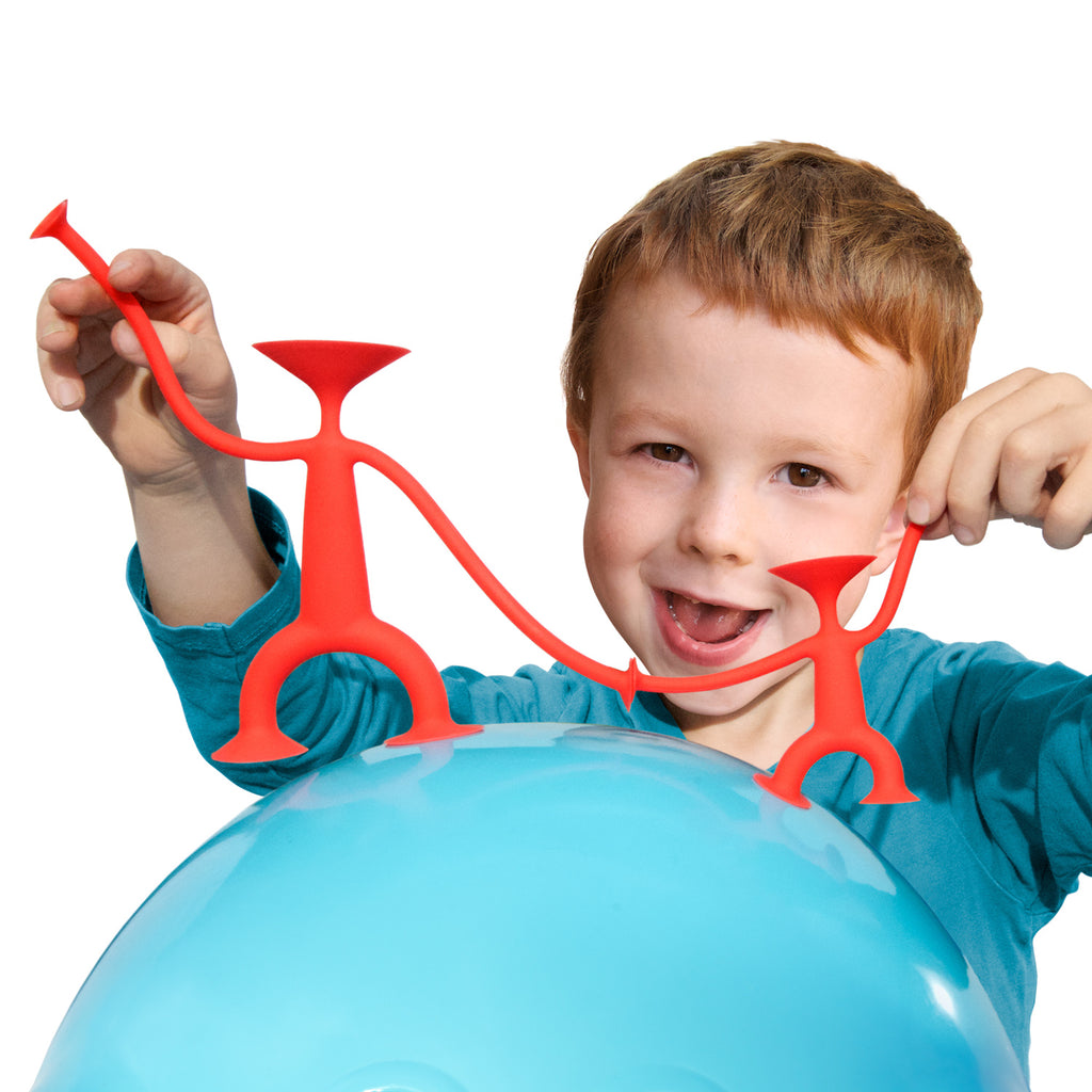 A joyful child holds red stick figures on a blue exercise ball. The child is smiling, creating a playful and cheerful vibe against a white background.