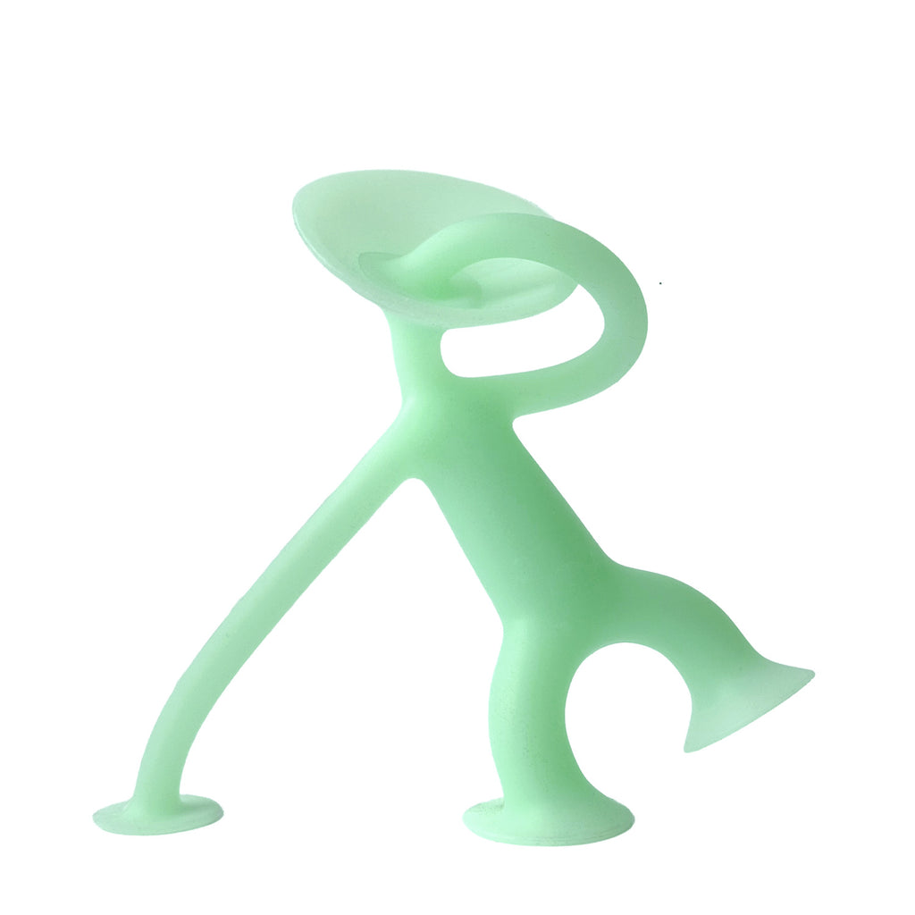 A light green, humanoid figure made of silicone. It has a suction cup head, elongated limbs, and a circular base, suggesting playful, modern design.