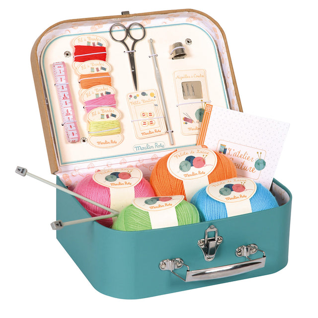 Moulin Roty kids sewing and knitting kit in teal suitcase with colorful yarn thread scissors and needles.