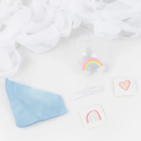 Unwrapped surprise ball contents including a joke slip, rainbow figure, temporary tattoos, tissue paper, and white streamer background.