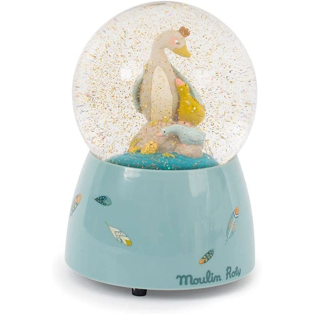 A snow globe containing a pastel-colored duck family stands on a light blue base adorned with colorful leaf illustrations. The brand name "Moulin Roty" is visible.