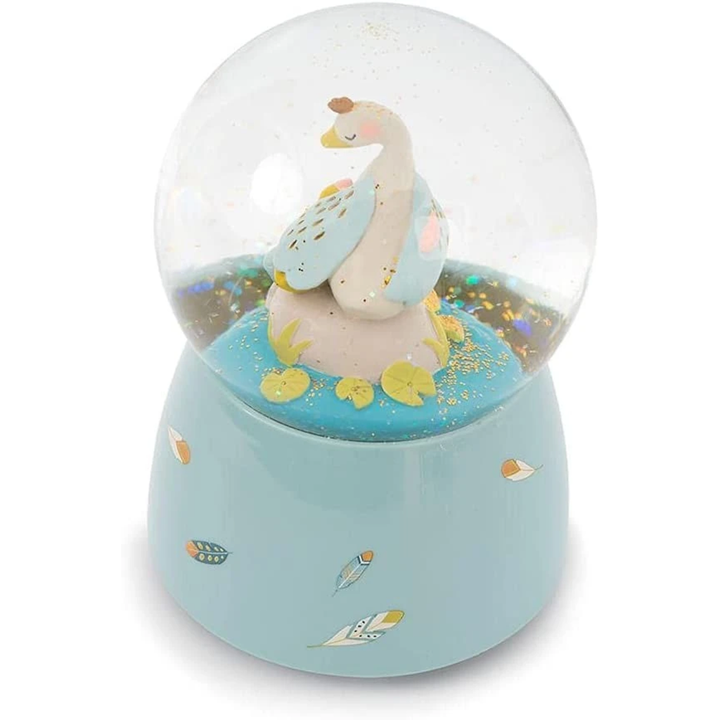 A snow globe containing a pastel-colored duck family stands on a light blue base adorned with colorful leaf illustrations. The brand name "Moulin Roty" is visible.