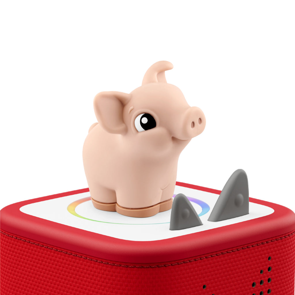 A cute, small pig figurine with a friendly expression stands on a red speaker box with two gray triangular buttons, conveying a playful tone.