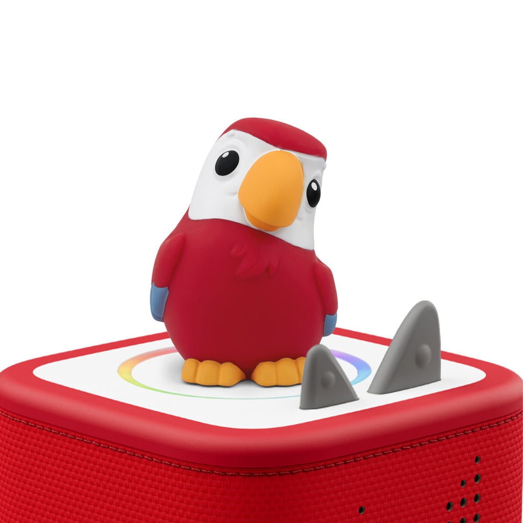 A vibrant red toy parrot with a large orange beak and white face perches on a red speaker box. The box features two gray triangular buttons.