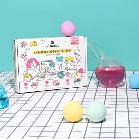 Nailmatic Bath Bomb Maker box on a gridded surface with colorful bath bombs and glassware.