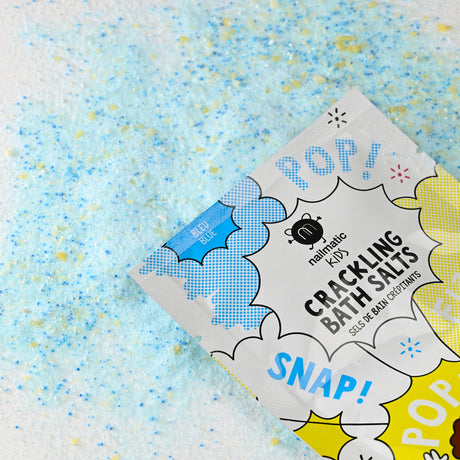 Colorful bath salts scattered on a white surface, with a playful package labeled "Crackling Bath Salts" featuring words like "POP" and "SNAP" in bright colors.