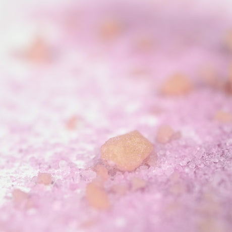 Close-up of pink and peach-hued coarse salt crystals on a smooth surface. The soft focus and pastel colors create a calm, serene atmosphere.