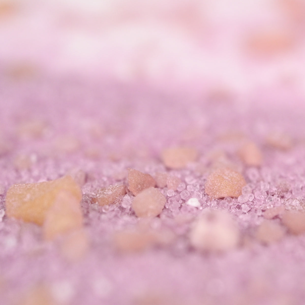 Close-up of pink salt crystals on a soft purple background. The image conveys a calm and soothing tone with its soft focus and pastel hues.