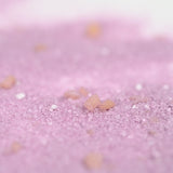 Close-up of coarse pink salt crystals scattered on a smooth, soft pink surface. The image evokes a calm and soothing atmosphere.