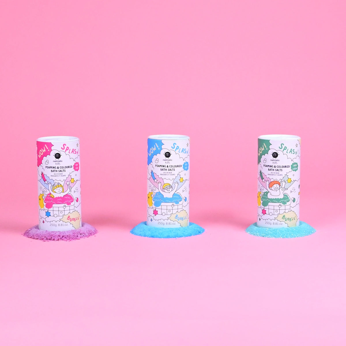 Three colorful bath salt containers stand on a pink background. Each has playful cartoon graphics, and vibrant salts spill out below: purple, blue, and green.