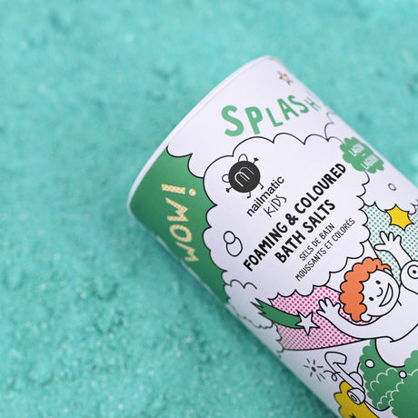 The image shows a cylindrical container of Nailmatic Kids foaming and colored bath salts against a textured turquoise background. The packaging features playful cartoon designs and bright colors, conveying a fun and cheerful mood.