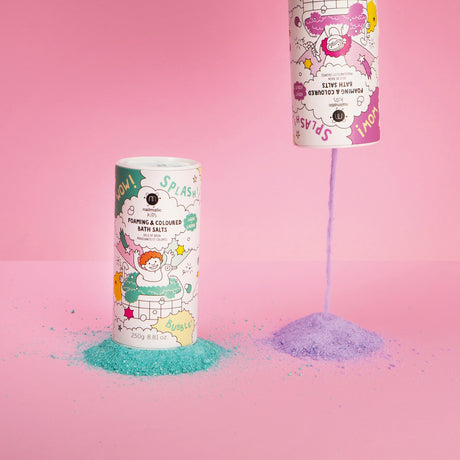 Two playful containers of foaming bath salts against a pink backdrop; one is upright with green salts, the other upside down pouring purple.