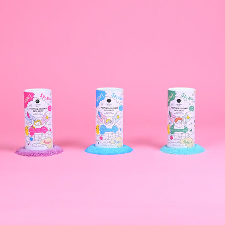Three vibrant bath salt containers are lined up against a pink background. Each has colorful designs and a small pile of matching salts beneath.