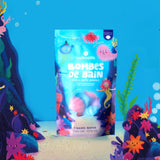 Brightly colored packaging of Nailmatic shell bath bombs on an underwater-themed background. The blue bag features playful, smiling sea creatures.