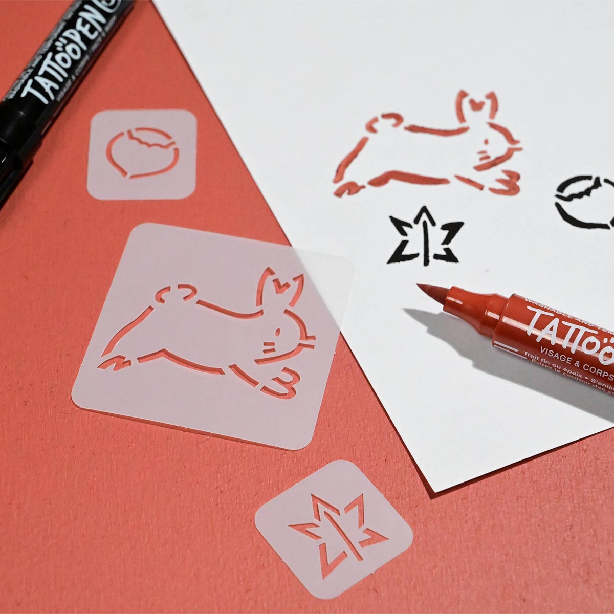 Stencil art supplies on red paper and white card. Includes a bunny and star stencil, used with black and red markers for tattoo designs.