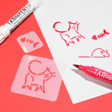 Red and pink stencils of a cat and fish are used on white paper with a pink tattoo marker and a white tattoo pen on a vibrant red background.
