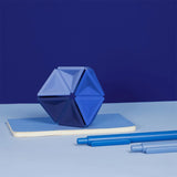 Blue silicone hexaflexagon fidget toy upright on a small notebook alongside two blue pens.
