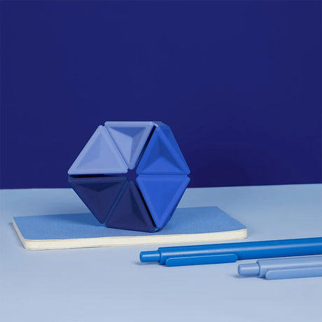 Blue silicone hexaflexagon fidget toy upright on a small notebook alongside two blue pens.
