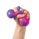 Hand squeezing a stress ball with a smooth, glossy surface, transitioning from purple to pink. The texture appears soft and elastic.