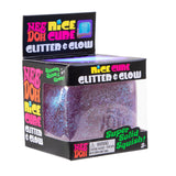 Packaging for a purple Nee Doh Nice Cube labeled "Glitter & Glow," featuring sparkles and text, "Super Solid Squish!" The box design is colorful and playful.