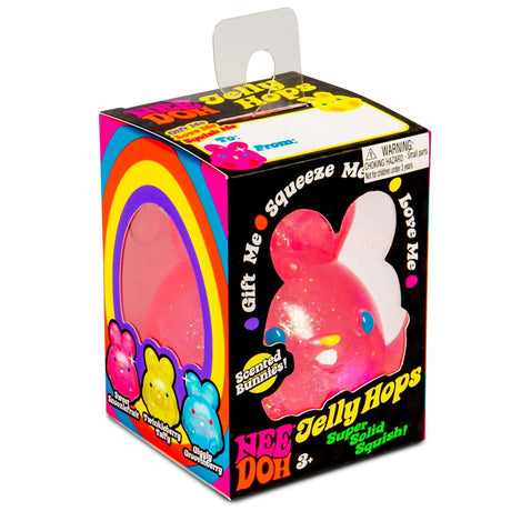Colorful box with a clear window reveals a sparkly pink bunny toy inside. Text reads "Nee Doh Jelly Hops, Scented Bunnies." Rainbow design and playful vibe.