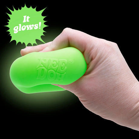 Hand squishing a glowing green NeeDoh sensory toy on a black background with "It glows!" text.