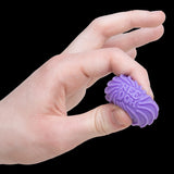 A hand gently squeezes a small, purple, textured fidget toy labeled "Nee-Doh" against a black background, conveying a sense of calm and focus.