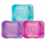 Three colorful NeeDoh stress balls are shown. The top ball is cyan, the left is purple, and the right is pink. Each has "NeeDoh" embossed on it.