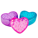 Three glittery heart-shaped soaps in purple, pink, and teal with messages "You Are Magic," "Be My Glow Up," and "Groovy." Bright and playful tone.