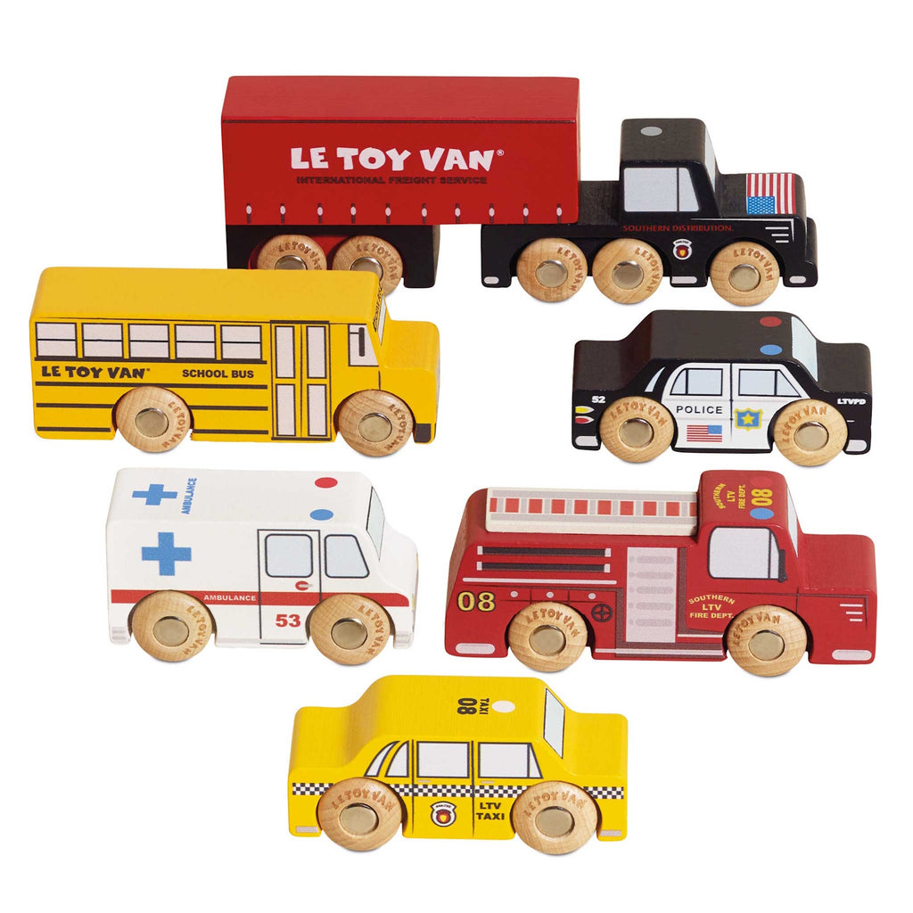 Wooden toy vehicles including a red semi-truck, yellow school bus, black police car, white ambulance, red fire truck, and yellow taxi, all with colorful details.