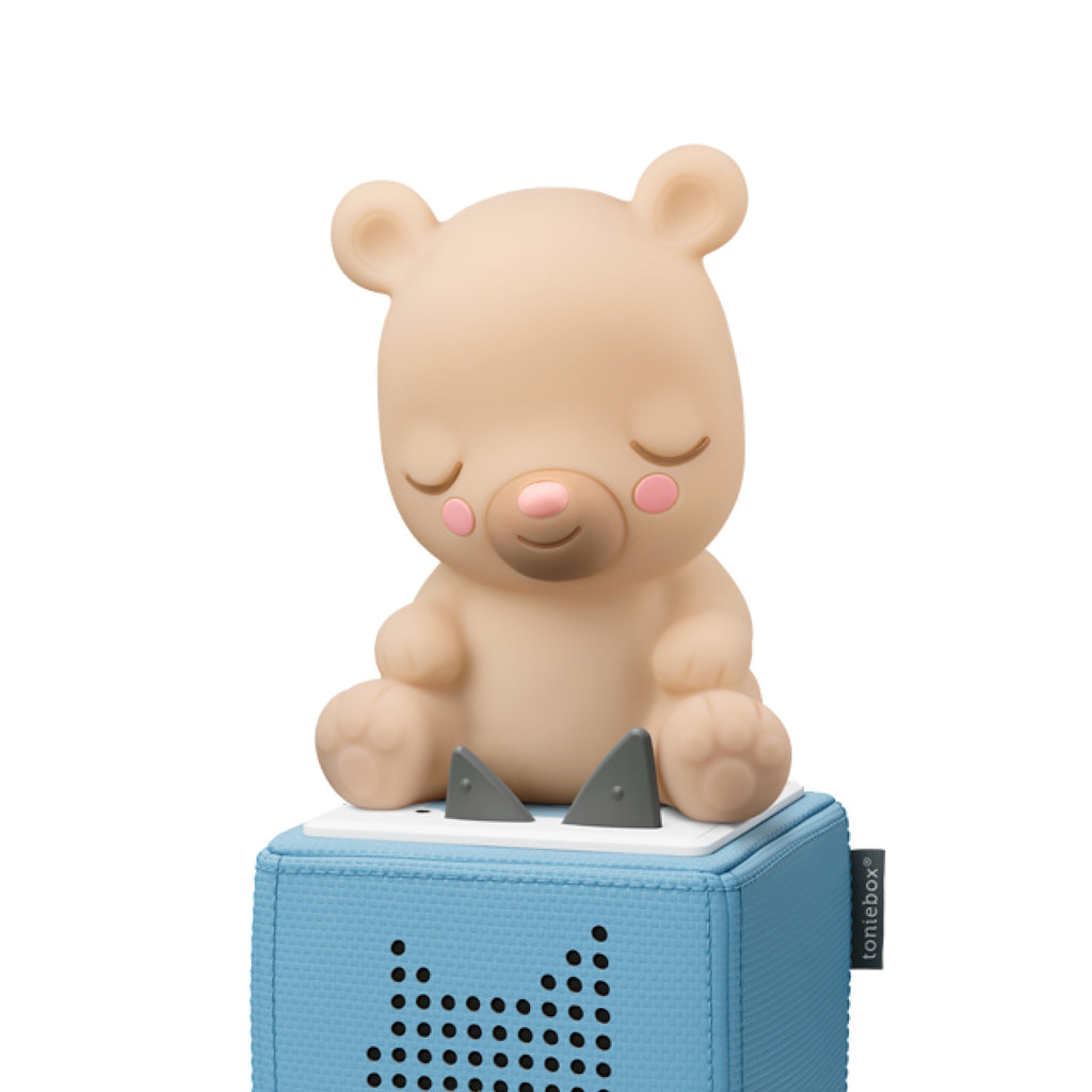 A cute, soft, beige bear figurine with a smiling face and closed eyes, sitting with its paws tucked under its body.