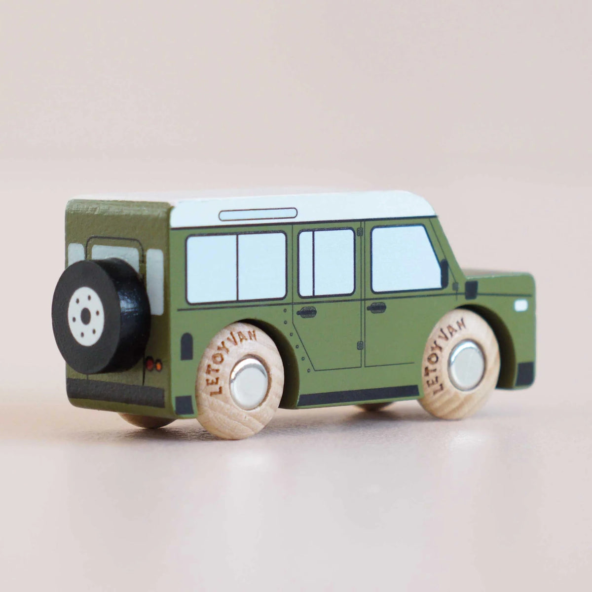 Rear three-quarter view of a green wooden toy car with a spare tire mounted on the back.