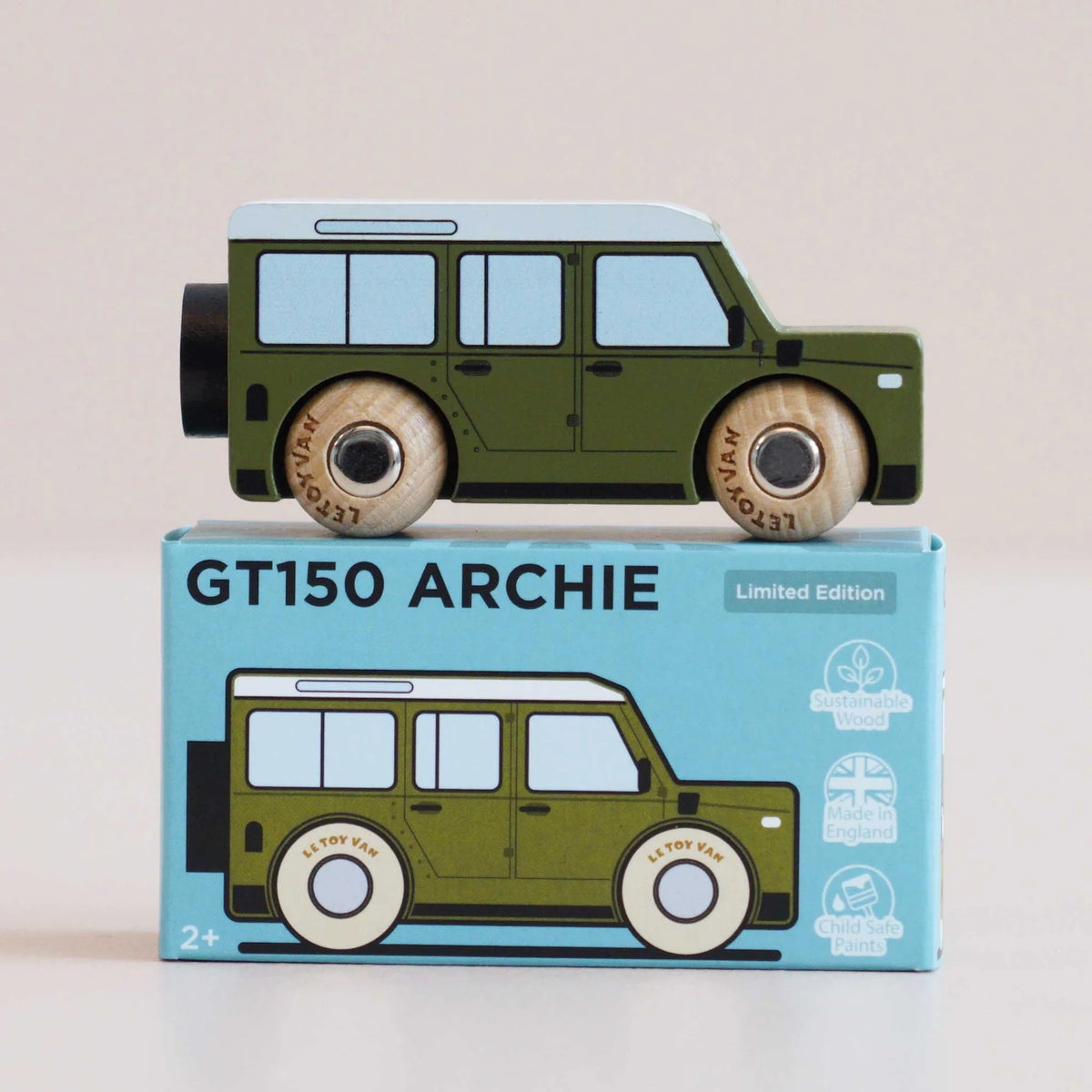 Side view of a green wooden toy car resting on top of its matching blue packaging box.