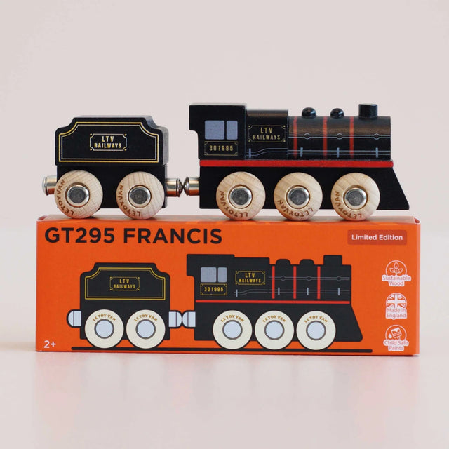 Black wooden toy steam train with natural wood wheels, resting on its orange packaging box labeled GT295 FRANCIS.