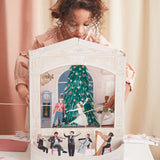 Child playing with a Nutcracker paper theater featuring dancing figures and a Christmas tree scene.