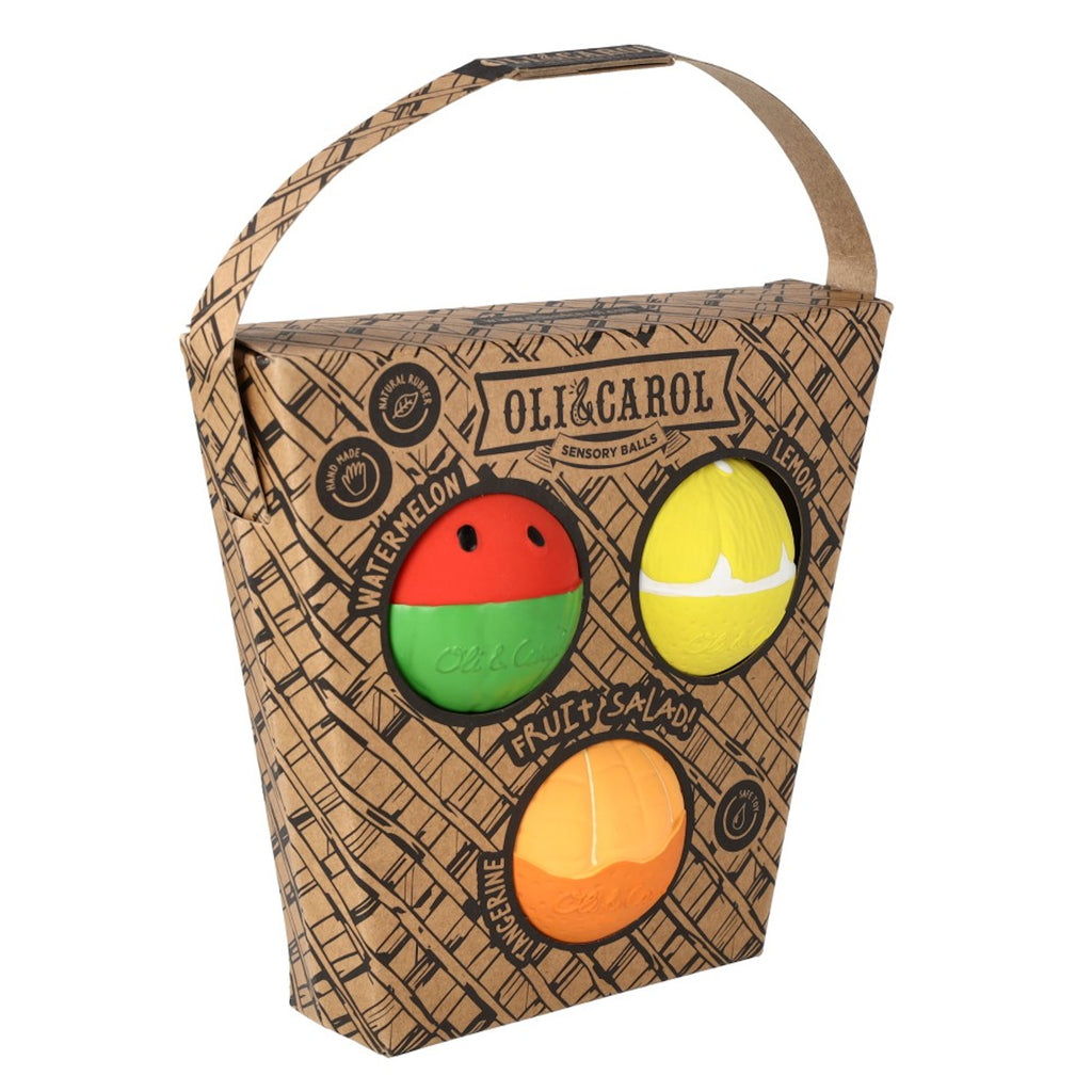 Packaging of sensory balls shaped like watermelon, lemon, and tangerine by Oli & Carol. The box is basket-patterned with a handle. Fun and playful design.