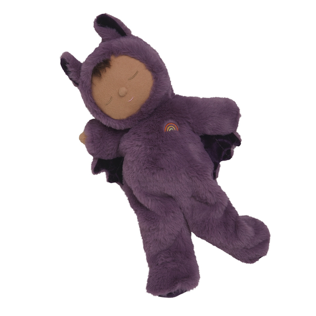A soft, plush doll in a purple bat costume, complete with wings and ears, lies peacefully with closed eyes. A small rainbow decorates its chest.