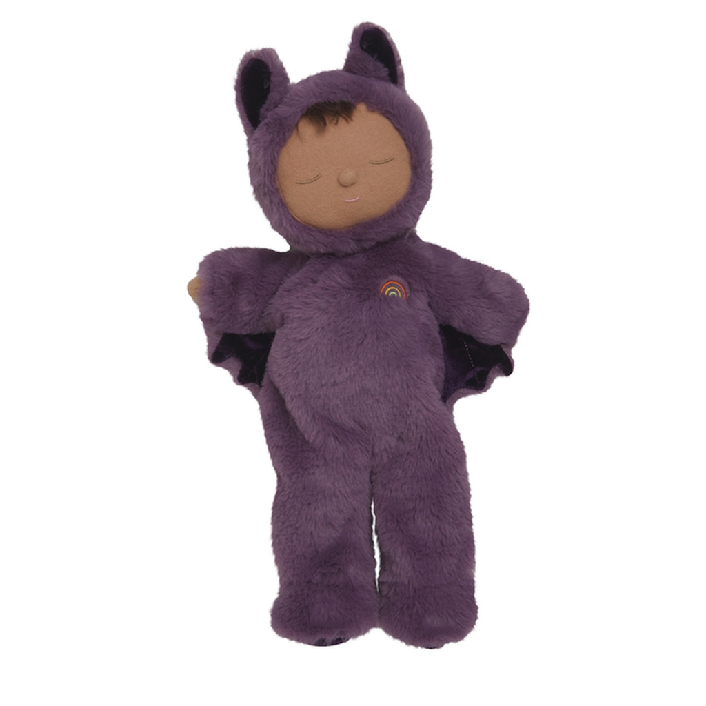 A soft, plush doll in a purple bat costume, complete with wings and ears, lies peacefully with closed eyes. A small rainbow decorates its chest.