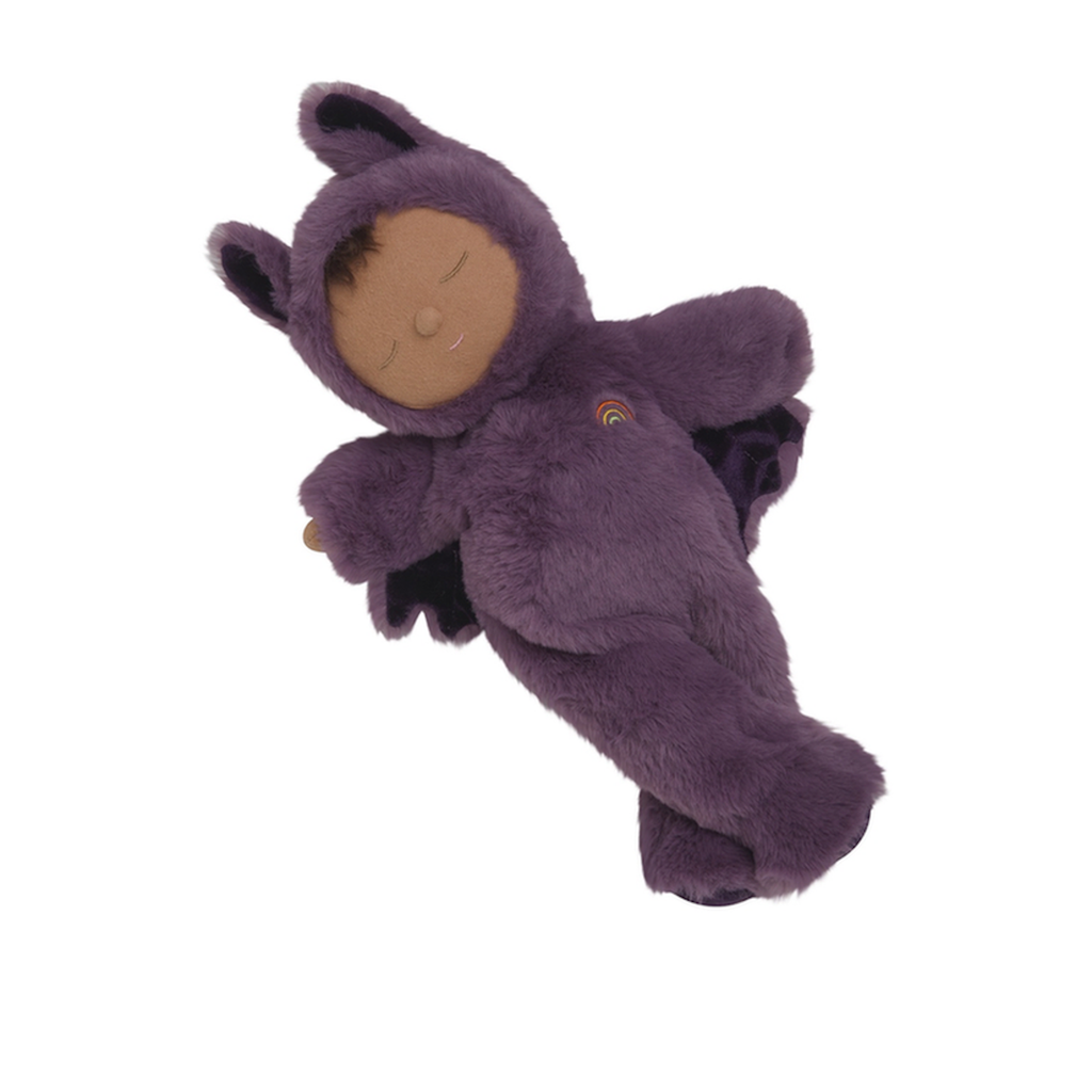 A soft, plush doll in a purple bat costume, complete with wings and ears, lies peacefully with closed eyes. A small rainbow decorates its chest.