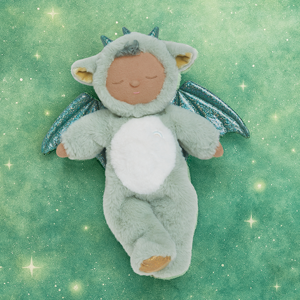 Plush baby doll in a green dragon onesie with sparkly wings and horns. The doll's eyes are closed, and it conveys a peaceful, sleepy expression.