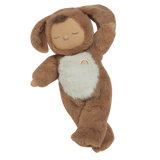 A plush toy with a brown, fluffy dog feature, closed eyes, and a serene expression. It features a white belly with a small embroidered rainbow.