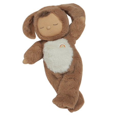 A plush toy with a brown, fluffy dog feature, closed eyes, and a serene expression. It features a white belly with a small embroidered rainbow.