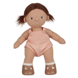 A soft, fabric doll with brown pigtails stands against a white background. It wears a pink romper and brown shoes, conveying a playful and charming tone.